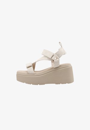Sandalia de plataforma beige con suela gruesa, dos correas ajustables sobre el pie y una alrededor del tobillo, con una pestaña para tirar en el talón.