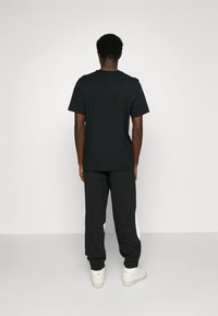 Czarna bawełniana koszulka połączona z czarnymi dresami z białymi akcentami. Gładka tekstura, luźny krój i klasyczny okrągły dekolt.