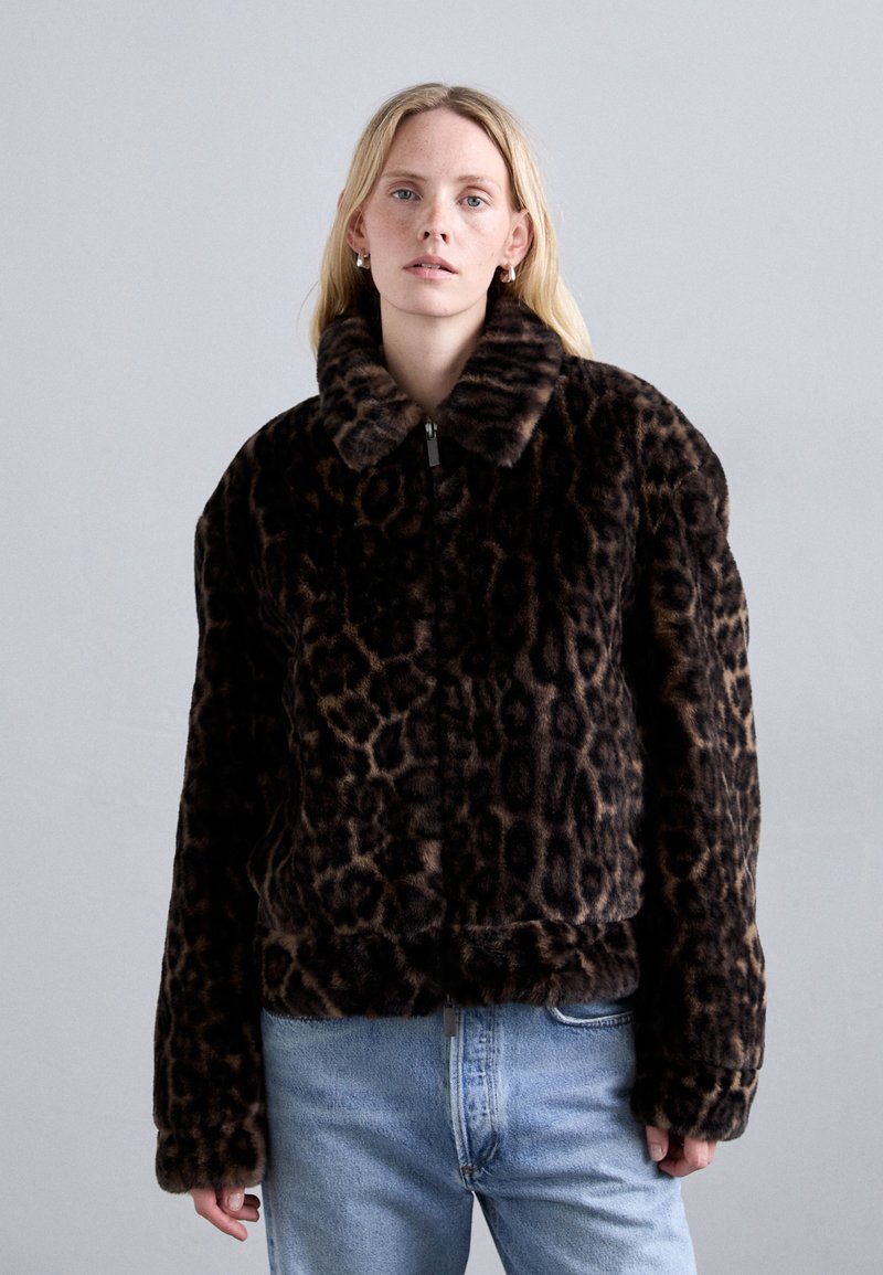 Leopard-print faux fur jacket with a collar, cropped design, black and brown colors, and zip closure, worn over light blue jeans.