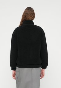 Μαύρο κοντό φλις μπουφάν με ψηλό γιακά, με υφή επιφάνειας και ελαστικά μανίκια, συνδυασμένο με γκρι cargo φούστα.