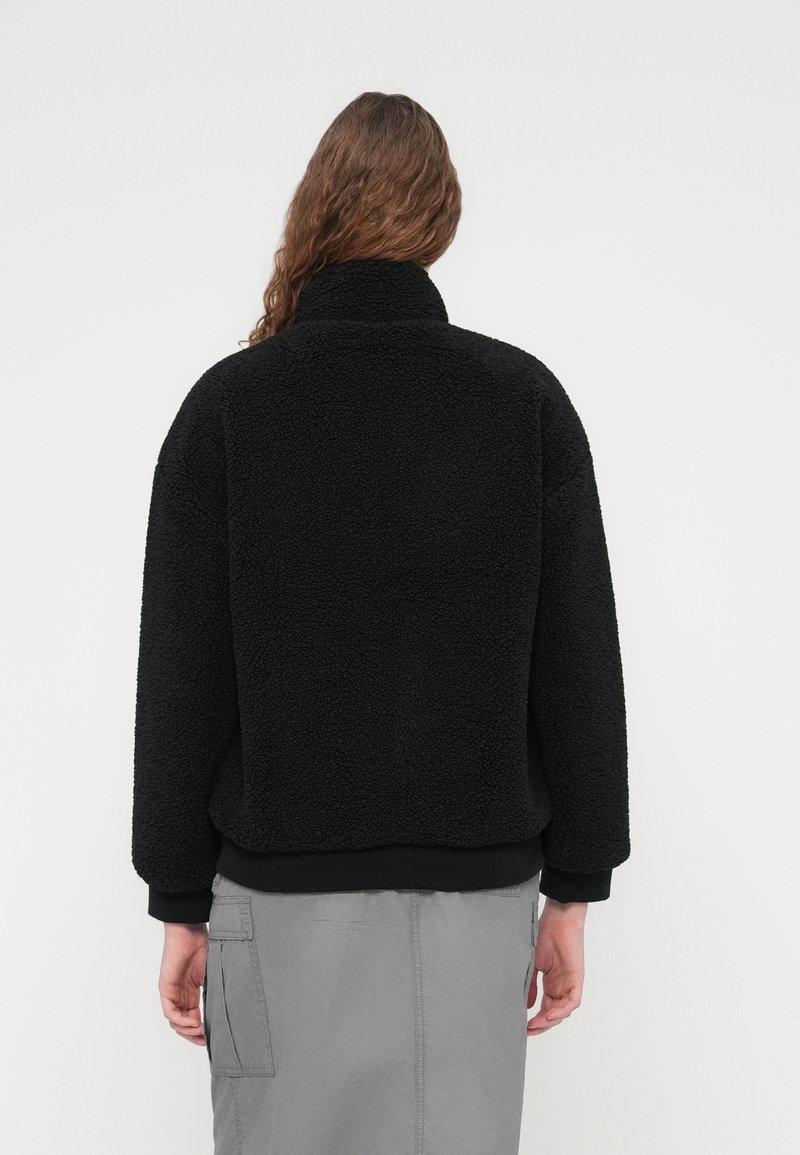 Sort cropped fleecejakke med høj krave, der har en tekstureret overflade og elastiske manchetter, kombineret med et gråt cargonederdel.