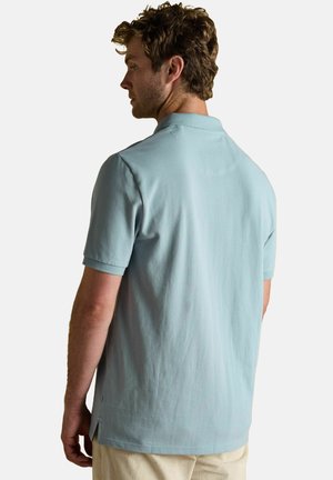 Helles blaues Polohemd aus weichem Stoff mit kurzen Ärmeln, gerade geschnittenem Saum und dezenten seitlichen Schlitzen, von hinten betrachtet.