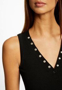 Top in cotone a righe nere con scollatura a V, dotato di bottoni a pressione metallici lungo la scollatura. Texture liscia con design aderente.