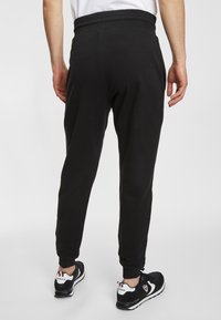 Zwarte joggerbroeken met een taps toelopende pasvorm, een elastische tailleband, gebundelde enkels en zijzakken, gecombineerd met zwarte sneakers met witte accenten.