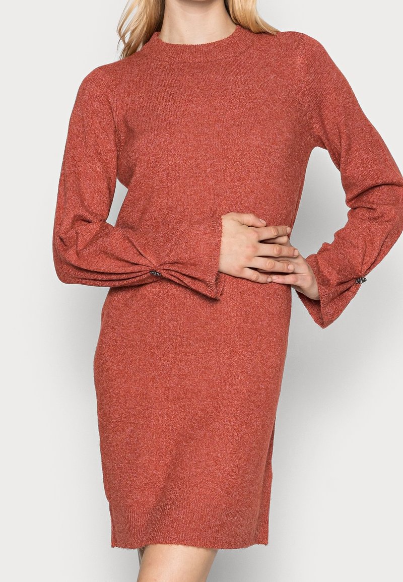 Kopparfärgad tröjkklänning med hög hals, långa ärmar, texturerad tyg och knappar på ärmarnas manschetter. Enkel, rak siluett.