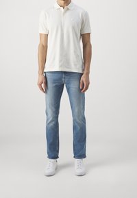 Vit polo skjorta med krage, kombinerad med ljusblå jeans och vita sneakers. Ren design, avslappnad passform och minimal branding.