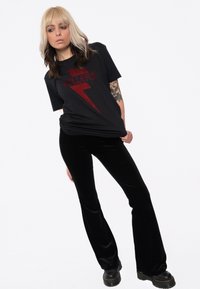 Black cotton t-shirt with a red lightning bolt design and "Killers" text, paired with black velvet flared pants and chunky black boots.