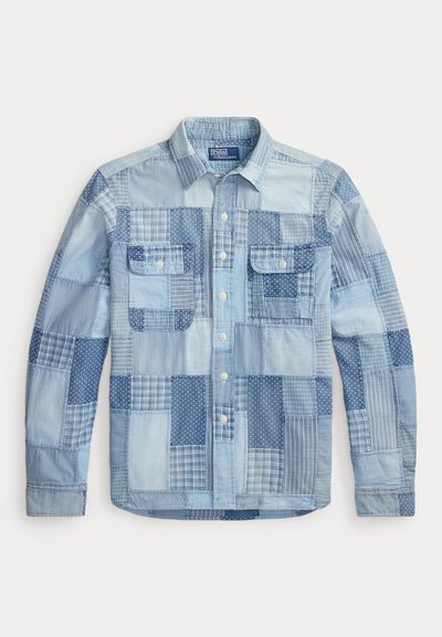 Chemise patchwork en denim bleu clair à manches longues, avec fermeture à boutons sur le devant et deux poches poitrine à boutons.