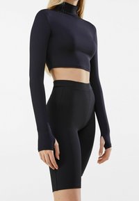 Top negro cortado con mangas largas y diseño de cuello alto, combinado con pantalones cortos de ciclista negros de talle alto. Tela suave y elástica.