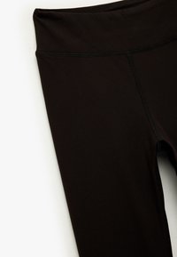 Zwarte sportleggingen gemaakt van rekbaar materiaal. Hoge tailleband met platte naden. Glad oppervlak, geen zichtbare patronen of hardwaredetails.