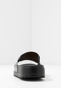 Sort slidesandal med en glat, blank overdel og en tekstureret sål med en tyk, komfortabel platform. Minimalistisk design, uden udsmykninger.