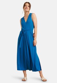 Blue sleeveless dress with a V-neck, belted waist, and flowing long skirt. Made of smooth fabric with a soft texture.
