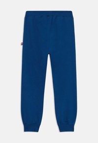 Navy blue sweatpants with a soft texture, elastic waistband, and tapered cuffs. Features a small logo tag on the side.