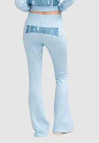 Pantalons de jogging évasés bleu clair avec "RELIGION" imprimé en grandes lettres au dos. Fabriqués en matériau doux et extensible avec une texture lisse.