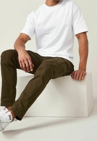T-shirt bianca in cotone abbinata a pantaloni cargo verde oliva. I pantaloni presentano tasche e una vestibilità slim, completati da sneakers bianche.