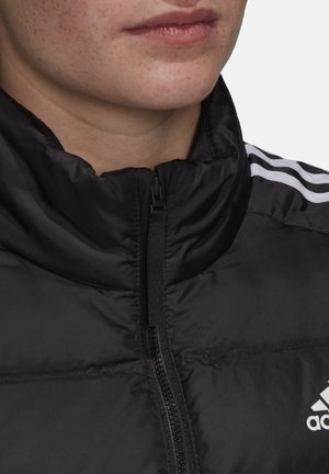 Close-up af nedre del af ansigt og hals iført en sort Adidas dunjakke med en central lynlås og hvide tre-stribe-detaljer på skulderen.