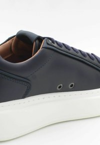 Sneaker in pelle blu navy con suola in gomma bianca, dotato di lacci blu scuro, occhielli in metallo e fodera interna marrone a contrasto.