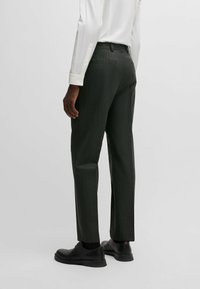 Pantaloni grigi scuri su misura con un sottile motivo a righe, caratterizzati da una vestibilità elegante e tasche posteriori, abbinati a scarpe nere eleganti.