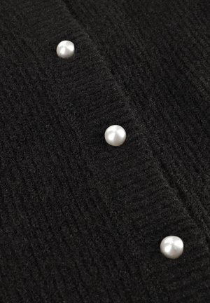 Zwarte gebreide cardigan met een textuur, voorzien van vijf grote, ronde, witte parelknoopsluitingen aan de voorkant, die het ribbelbreipatronen accentueren.