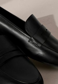 Mocassini in pelle nera con finitura liscia, caratterizzati da una banda decorativa sulla parte anteriore e dettagli di cucitura discreti. Design con punta arrotondata.
