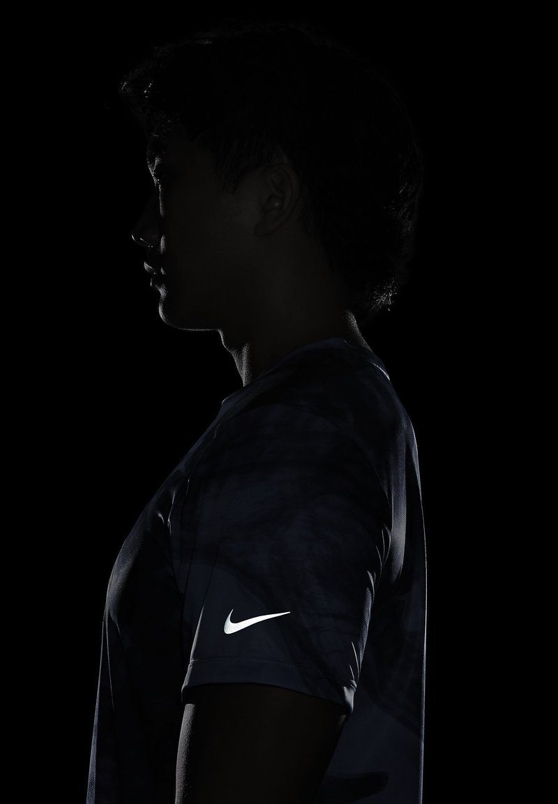 T-shirt de sport Nike en bleu marine avec un motif texturé ; présente un logo blanc sur la manche gauche. Le fond est noir pour le contraste.