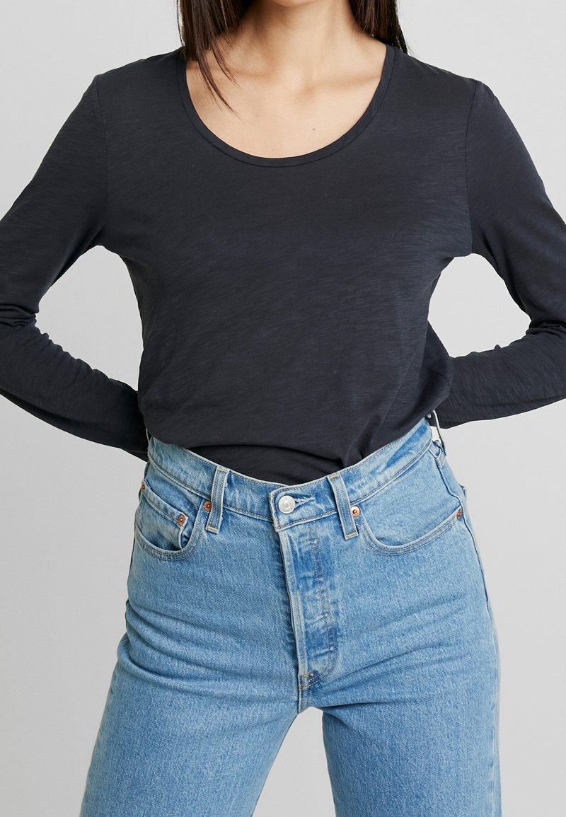 Långärmad, mörkgrå topp med rundad halsringning, kombinerad med högmidjade ljusblå denimjeans som har minimal sömnad och kopparfärgade detaljer.