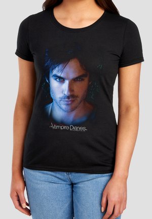 Woman wearing black T-shirt with a blue-lit male face from The Vampire Diaries and the show’s logo below the image.
