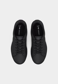 Ζεύγος μαύρων χαμηλών αθλητικών παπουτσιών Lacoste με μαύρα κορδόνια και εσωτερικές σόλες Ortholite, εμφανιζόμενα από πάνω σε λευκό φόντο.