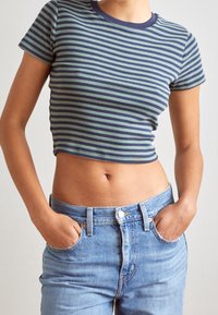 Randig kort topp i grön och marinblå, korta ärmar, med rund halsringning. Matchas med högmidjade ljusblå jeans.