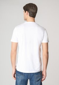 T-shirt bianco a maniche corte realizzato in cotone, con colletto girocollo classico e design semplice, indossato con jeans blu.