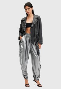 Must musta biker-jakk mustast nahast hõbedaste nupukestega, kitsas must crop top, läikivad hõbedased cargo-püksid ja mustad kontsakingad.