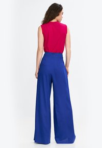 Czerwona bluzka bez rękawów i niebieskie spodnie z wysokim stanem i szerokimi nogawkami. Bluzka ma gładką fakturę; spodnie charakteryzują się dopasowanym krojem i czystymi liniami.