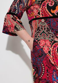 Bunt gemustertes Kleid mit Paisleymuster in Rot, Schwarz und Blau. Der Stoff ist weich, mit lockerer Passform und Dreiviertel-Ärmeln im Glockenstil.
