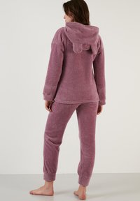 Set de loungewear pufoș, de culoare lavandă, cu glugă și accente în formă de urechi de urs. Bluza are mâneci lungi, iar pantalonii au manșete elastice.