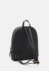 Black fabric backpack with a rounded shape, gold zip closure, two adjustable straps, and a top handle. Smooth texture and simple design.