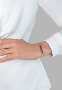 Bracelet en argent avec des pierres précieuses rouges alternées et des accents clairs, présentant un design élégant et fin avec une texture lisse.