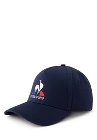 Gorra de béisbol azul marino hecha de tela, con un logo de ave blanca y acentos rojos/azules. Visera curvada y correa trasera ajustable.