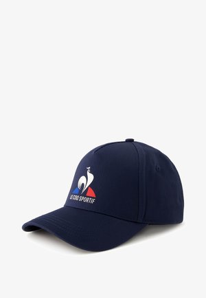 Gorra de béisbol azul marino hecha de tela, con un logo de ave blanca y acentos rojos/azules. Visera curvada y correa trasera ajustable.