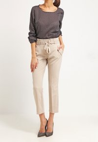 Blusa scura a pois abbinata a pantaloni beige su misura con cintura in vita e lunghezza cropped, completata da tacchi alti grigi.