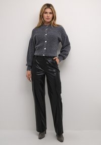Mørk grå tekstureret cardigan med store knapper, kombineret med glansfulde sorte brede bukser og glitrende spidse hæle.