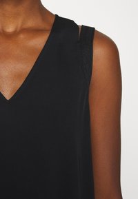 Top negro sin mangas con diseño de escote en V, fabricado en tela suave y con detalles de costura sutil a lo largo del escote y los hombros.
