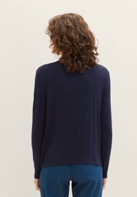 Marineblauw lange mouw top met een gladde textuur en een relaxte pasvorm, voorzien van een ronde halslijn en een rechte zoom, gecombineerd met blauwe broek.