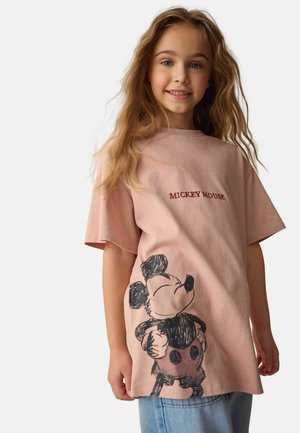 Svetloružové tričko s veľkým čiernym náčrtom Mickeyho Mousa, s textom "MICKEY MOUSE" tmavomodrej farby nad dizajnom.