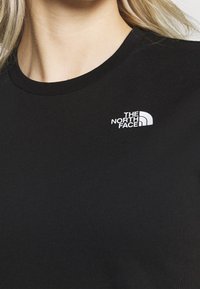 Černé bavlněné tričko s kulatým výstřihem a bílým logem "The North Face" na levé straně hrudníku. Hladká textura, přiléhavý střih.