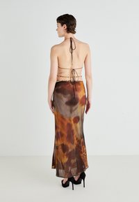 Satin halterkleita ar dzīvnieku drukas rakstu siltos brūnos un oranžos toņos. Tam ir aizmugures saites un slāņota dizaina, valkāta ar melniem augstiem papēžiem.