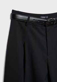 Črne hlače z gladko površino, ki imajo širok pas z sijočo črno obdelavo in nagubano sprednjo podrobnost.