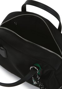 Μαύρη τσάντα χεριού με ασημί φερμουάρ εντελώς ανοιχτή, μαύρες ραμμένες λαβές και ένα μαύρο-άσπρο κορδόνι προσαρτημένο σε ένα ασημί δαχτυλίδι.