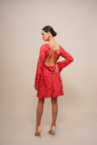 Kleid mit rotem Blumenmuster, langen Ärmeln und offenem Rücken, ausgestattet mit einer Bindeschleife. Das Modell trägt nudefarbene High-Heels.