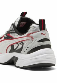 Gray and white athletic sneaker with red accents, textured mesh upper, padded collar, and black outsole. Features a pull tab on the heel.