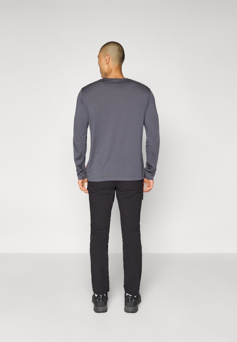 Graues Langarmshirt mit einem Rundhalsausschnitt, getragen mit schwarzen Hosen und dunklen Schuhen, von hinten vor einem schlichten Hintergrund gezeigt.